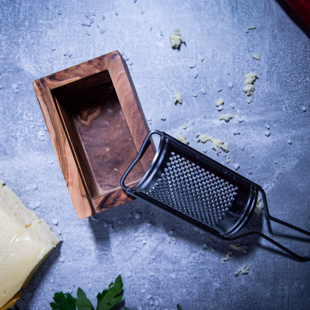 kaesereibe-aus-olivenholz-mit-kaesestueck-liegend-auf-tisch-von-oben-fotografiert