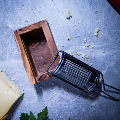 kaesereibe-aus-olivenholz-mit-kaesestueck-liegend-auf-tisch-von-oben-fotografiert