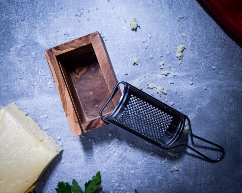 kaesereibe-aus-olivenholz-mit-kaesestueck-liegend-auf-tisch-von-oben-fotografiert
