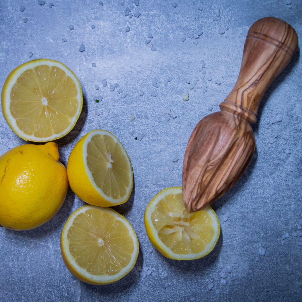 zitronenpresse-aus-olivenholz-mit-aufgeschnittenen-zitronen-von-oben-fotografiert